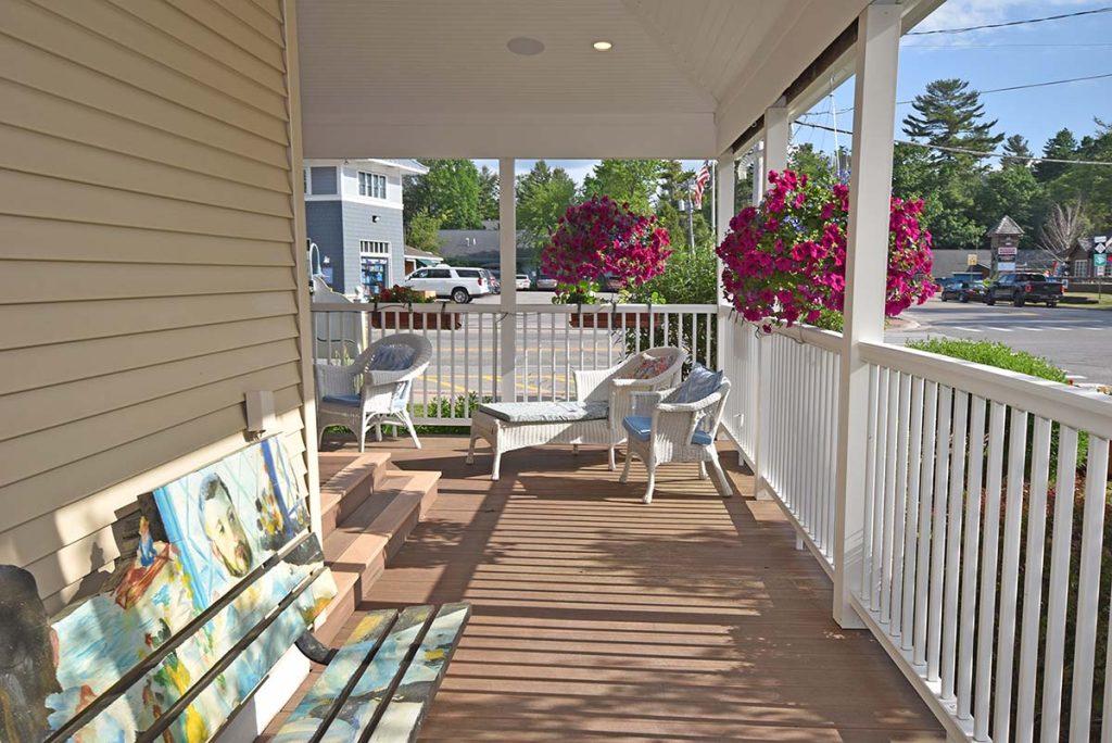 The front porch at Glen Arbor Bed & Breakfast and Condos, with white wicker chairs, hanging petunias, and downtown across the street.