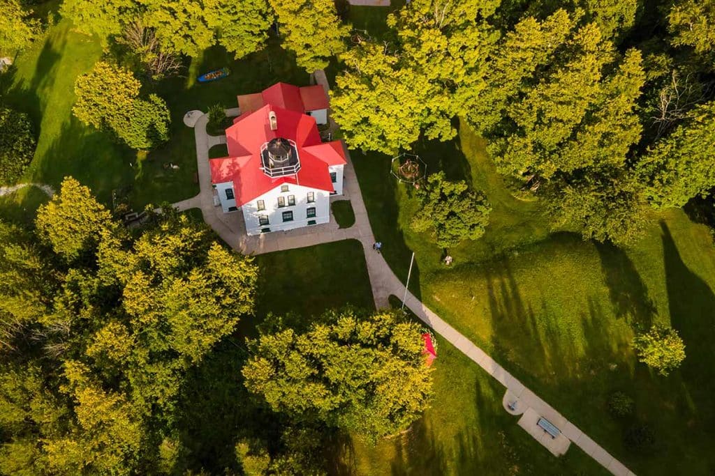 Aerial view of the Grand Traverse Lighthouse at the tip of the Leelanau Peninsula, with its red roof set in surrounding forest.