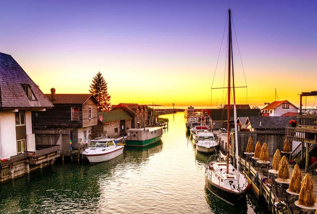 Sunset over Leland's Fishtown harbor, with sailboats and historic fishing shanties along the water.